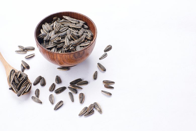 A wooden bowl of sunflower seeds with a wooden spoon